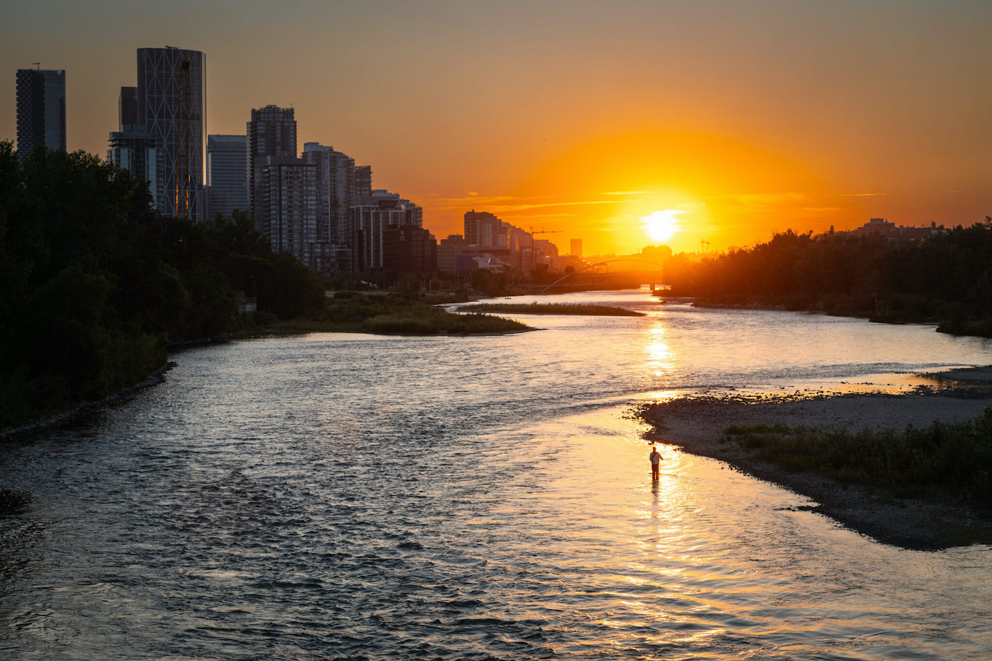 The sun sets in the distance of a lake and a cityscape.