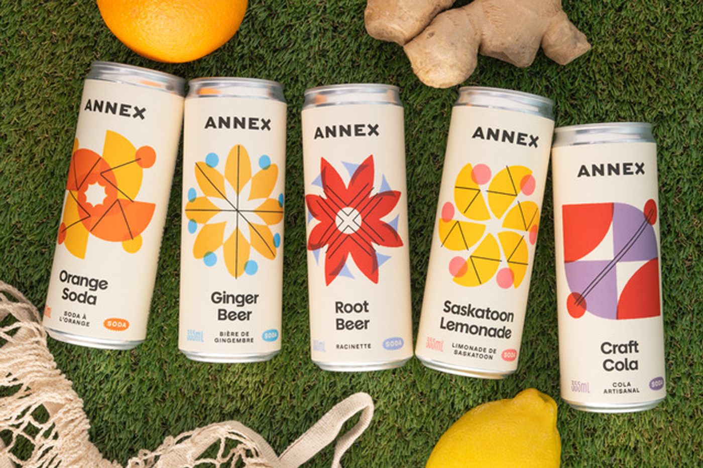 Five soda cans that have a clean design with bold shapes on the label. The soda cans are pictured with a lemon, a piece of ginger and an orange.